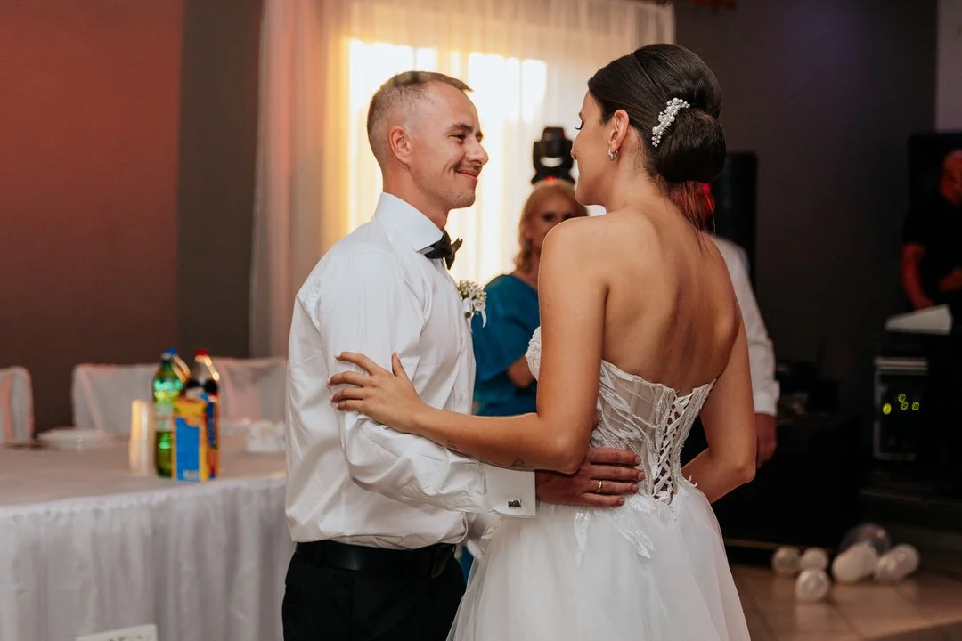 A bride and groom dance together at their wedding reception, holding each other and smiling, in a decorated indoor venue.