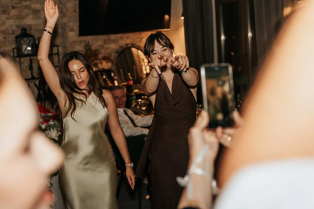 Two women dancing and having fun at a party, with one woman capturing the moment on her phone.