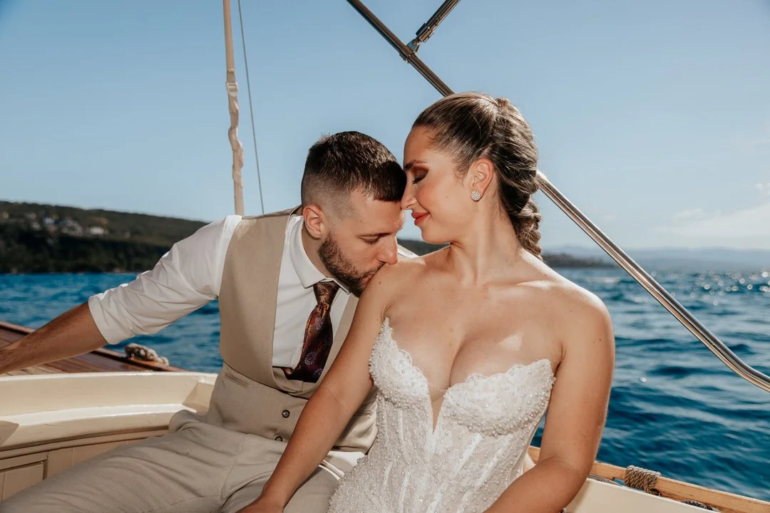 Newlywed couple on a boat cruising around Opatija and Volosko on Kvarner Bay, with the groom kissing the bride on her shoulder during their wedding photoshoot.