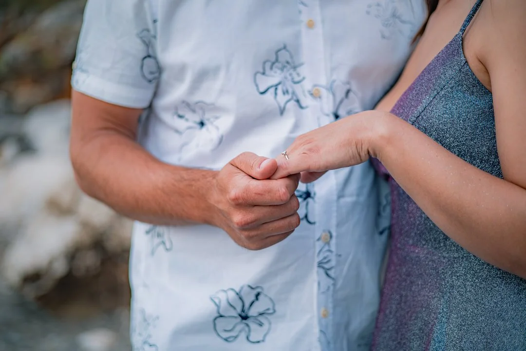 A man and woman holding hands; the man is wearing a light shirt with floral print, the woman is wearing a sleeveless shimmering dress.