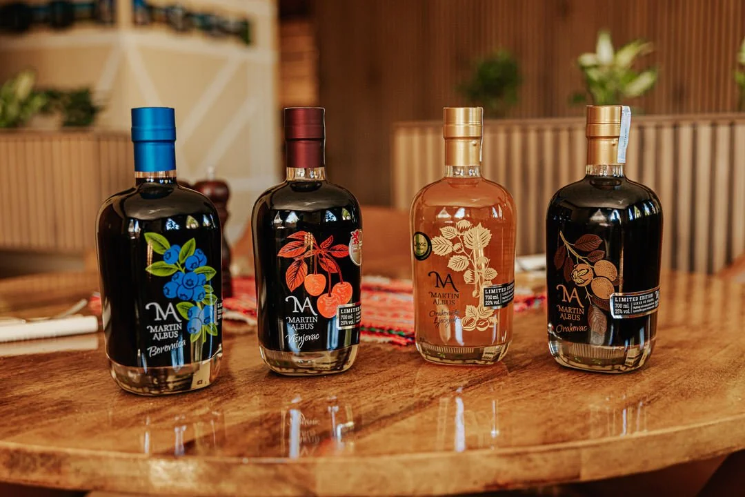 Four bottles of Martin Albus liquor on a wooden table, each with colorful botanical labels and metallic caps, in a cozy indoor setting.