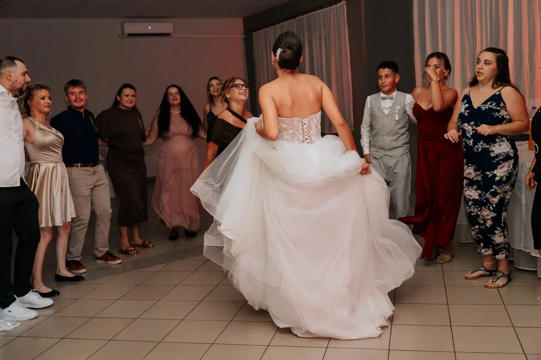 Bride dancing in a white wedding dress with guests around her at a reception.
