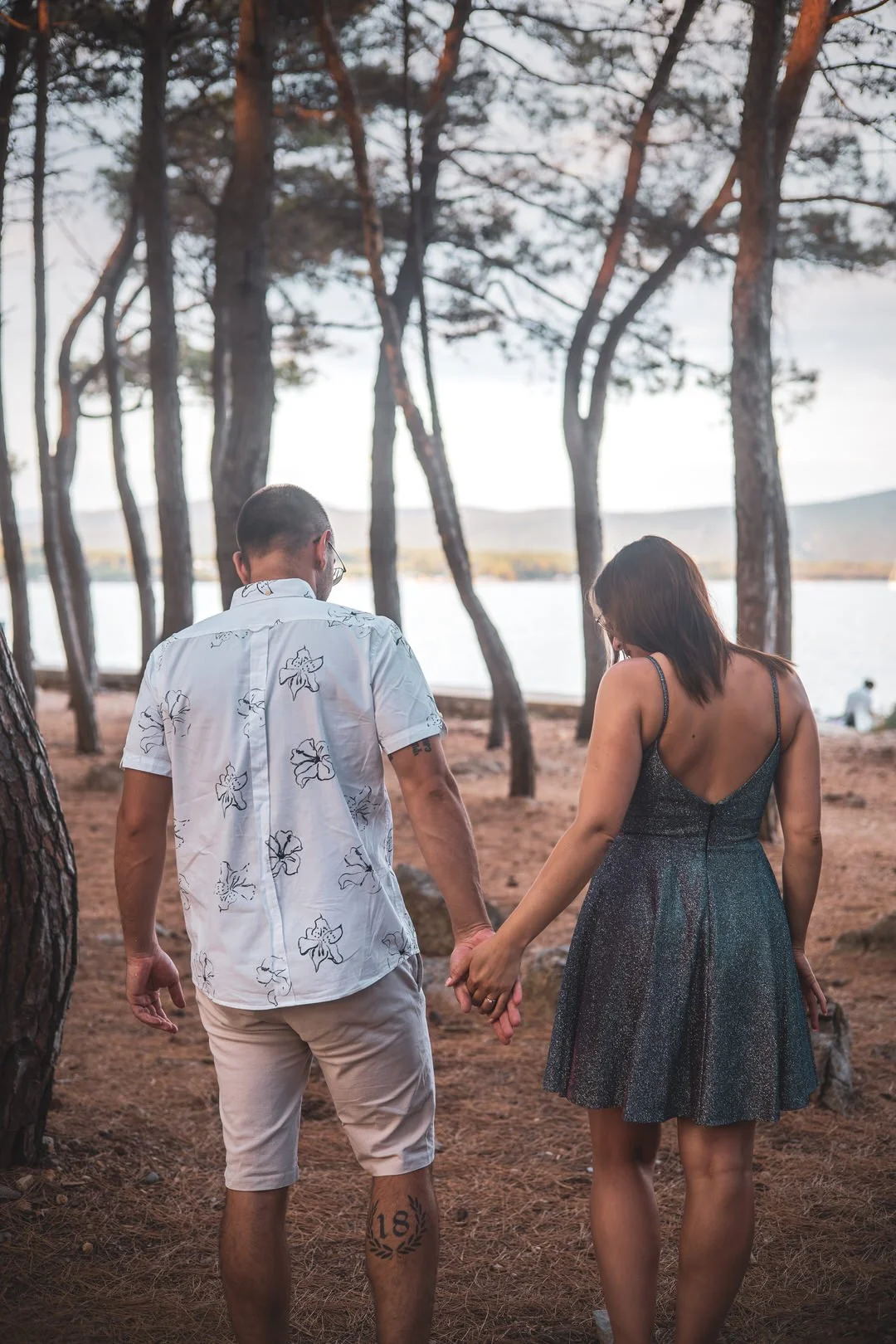 A couple walking hand in hand through a wooded area near the Adriatic Sea during daytime at Plav Beach, Krk Island, Croatia.