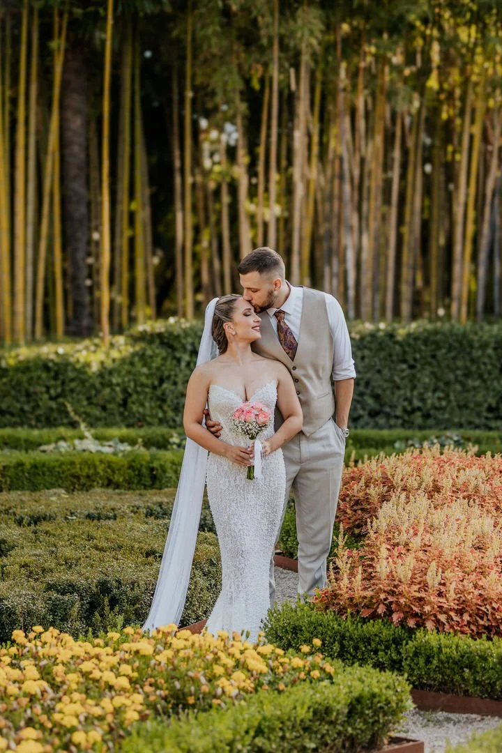 Newlywed couple sharing a tender moment in Park Angiolina, Opatija, Kvarner, surrounded by lush greenery and colorful flowers.