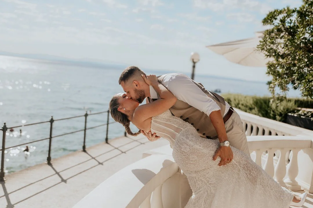 Bride and groom sharing a romantic kiss on a balcony overlooking the sea in front of Hotel Kvarner in Opatija, Kvarner, Croatia, during their wedding session.