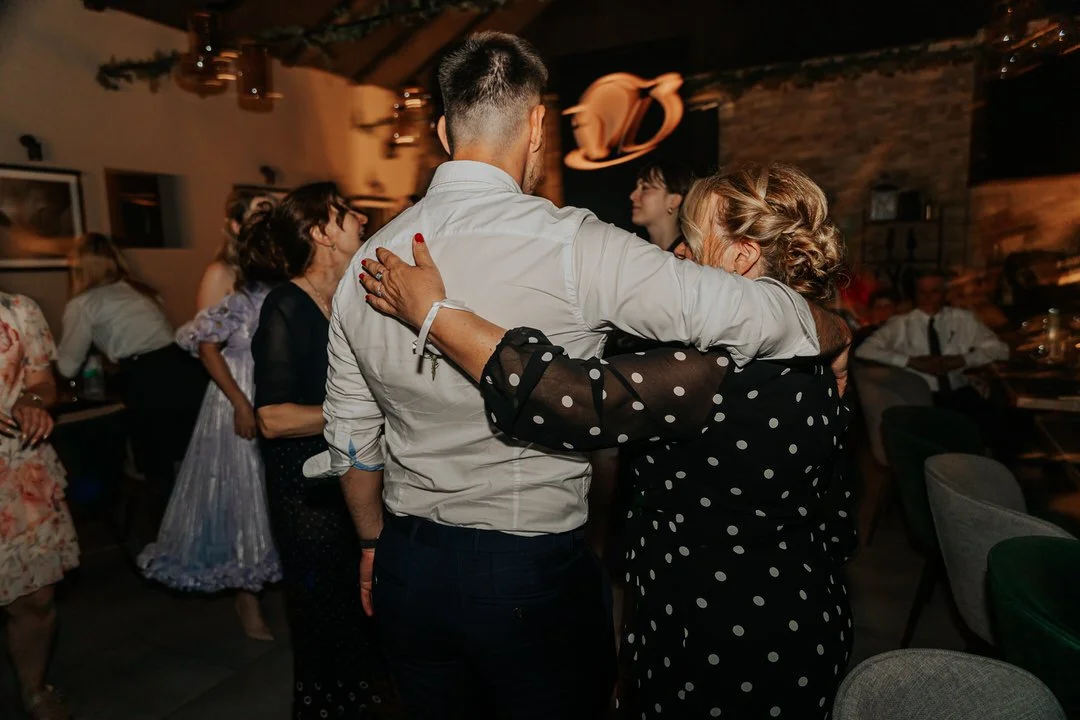 People dancing and hugging in a dimly lit indoor Dunavski raj venue, with brick walls and hanging lights.