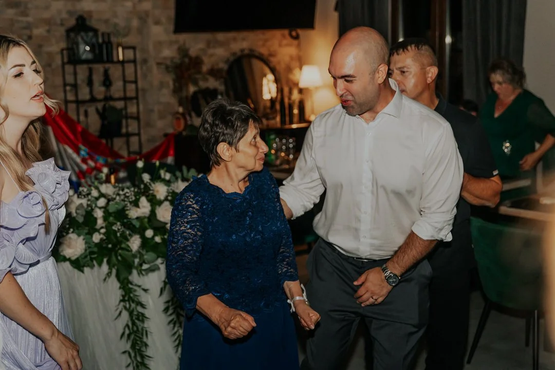 Group of people socializing indoors, with a floral arrangement and romantic lighting in the background.