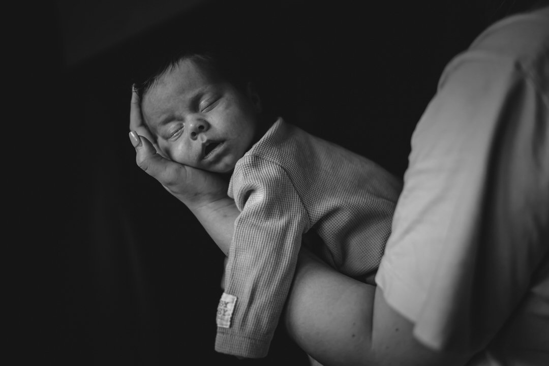 A person holding a sleeping baby close, with the baby’s face resting on the person’s hand.
