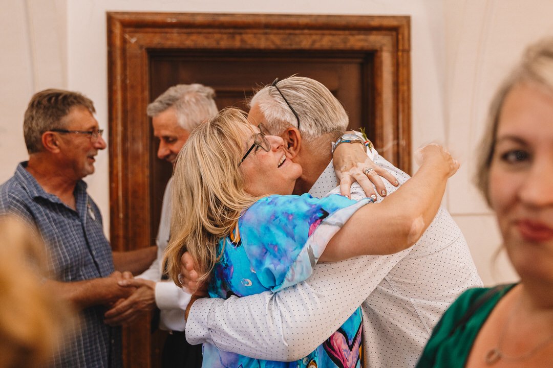 A group of people hugging and greeting each other at a social gathering or celebration in an indoor setting.