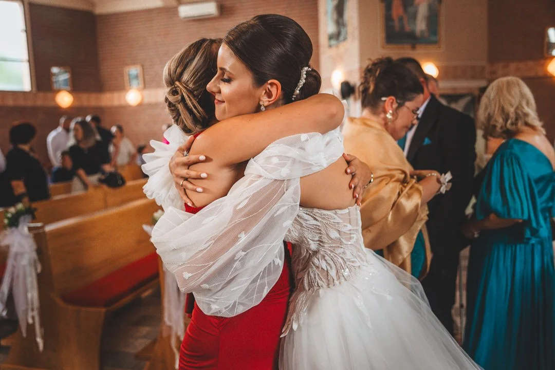 Two women, one in a wedding dress, hugging at a wedding reception in a church.
