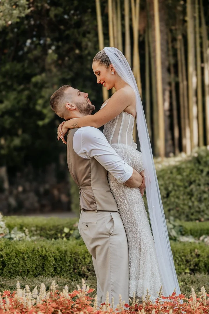Bride and groom sharing a joyful moment in Park Angiolina, Opatija, Kvarner, with the groom lifting the bride among tall bamboo shoots during their wedding photoshoot.