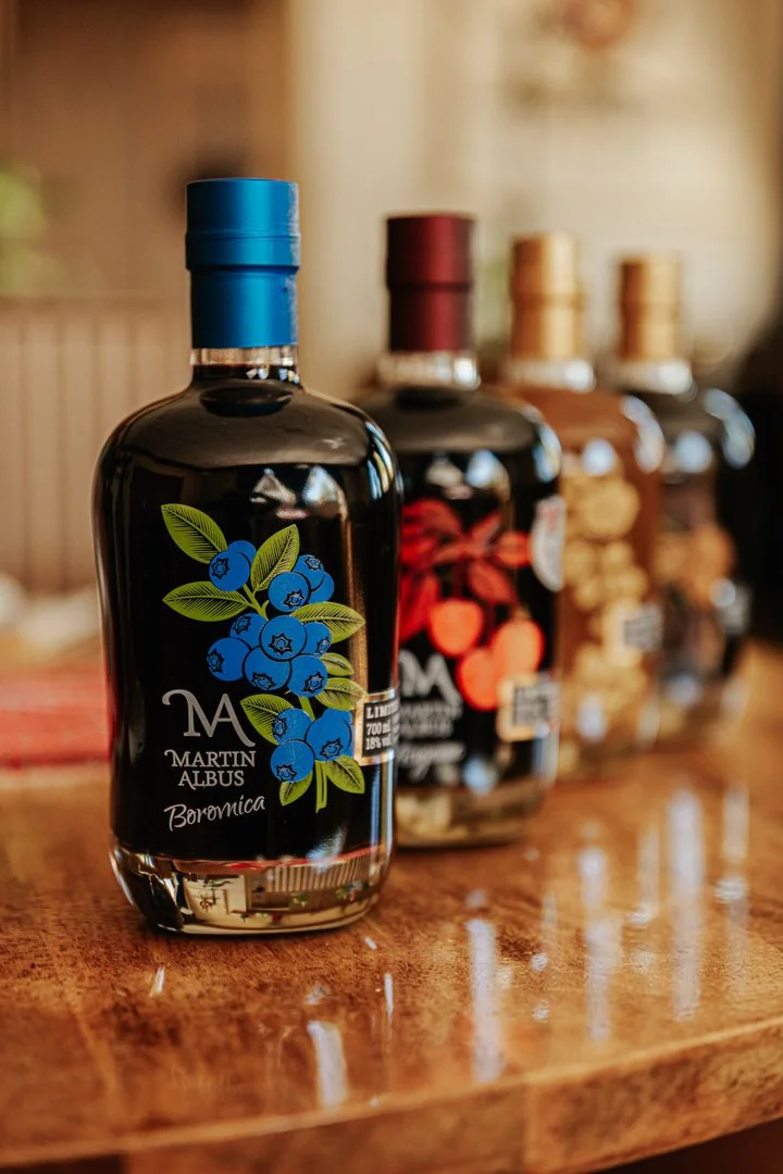 A bottle with a blue cap and label featuring blueberries and green leaves,MARTIN ALBUS on a wooden surface with other bottles in the background.