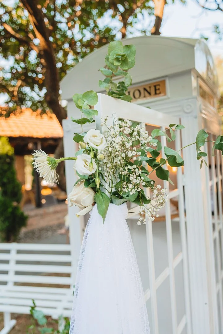 White mailbox decorated with a floral bouquet and white tulle, set outdoors with trees and a house in the background.