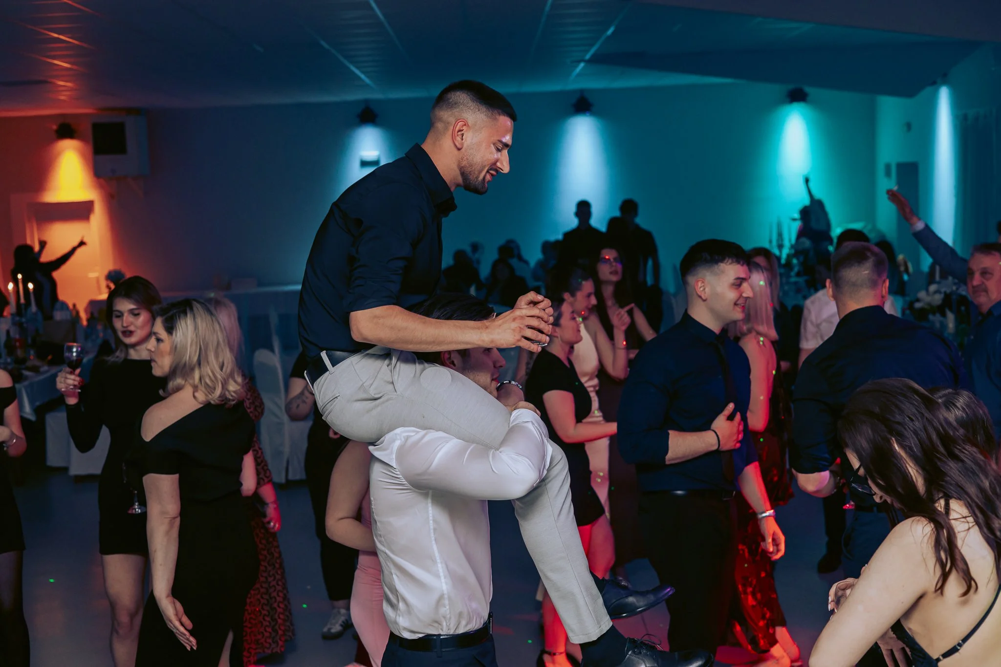 People dancing and socializing at an indoor event with colorful lighting at prom