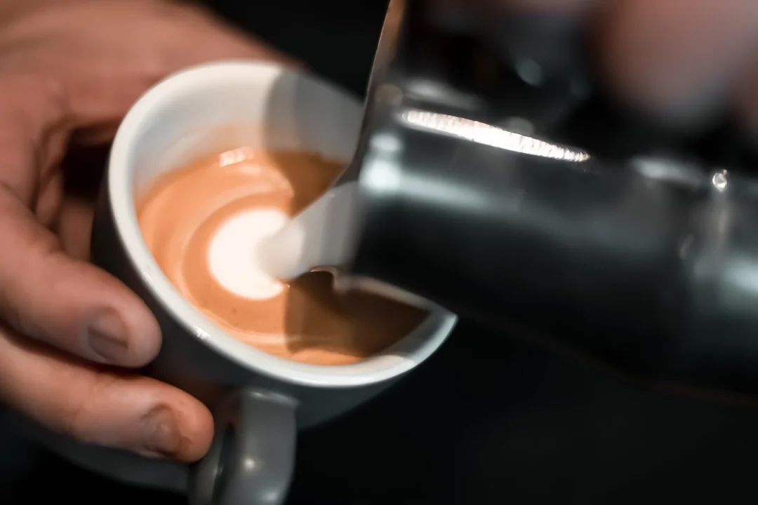 Barista pouring steamed milk into a cup of espresso, creating latte art in Izakaya Zagreb Croatia