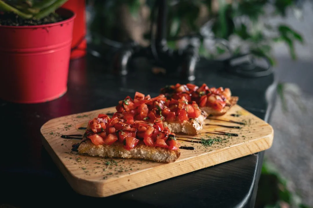 Three slices of bruschetta topped with diced tomatoes and herbs on a wooden serving board.