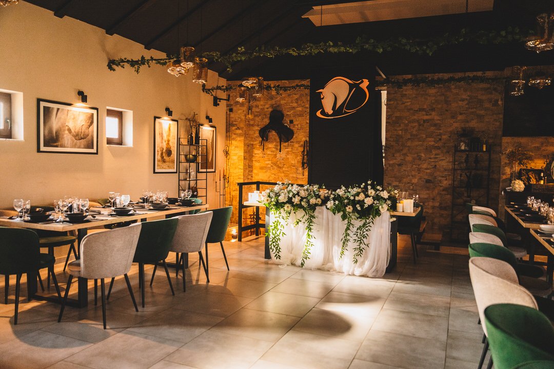 A decorated dining area at Dunavski Raj wedding venue, with tables set for a formal event, floral arrangements, candles, and elegant lighting in a room with brick walls and artwork.