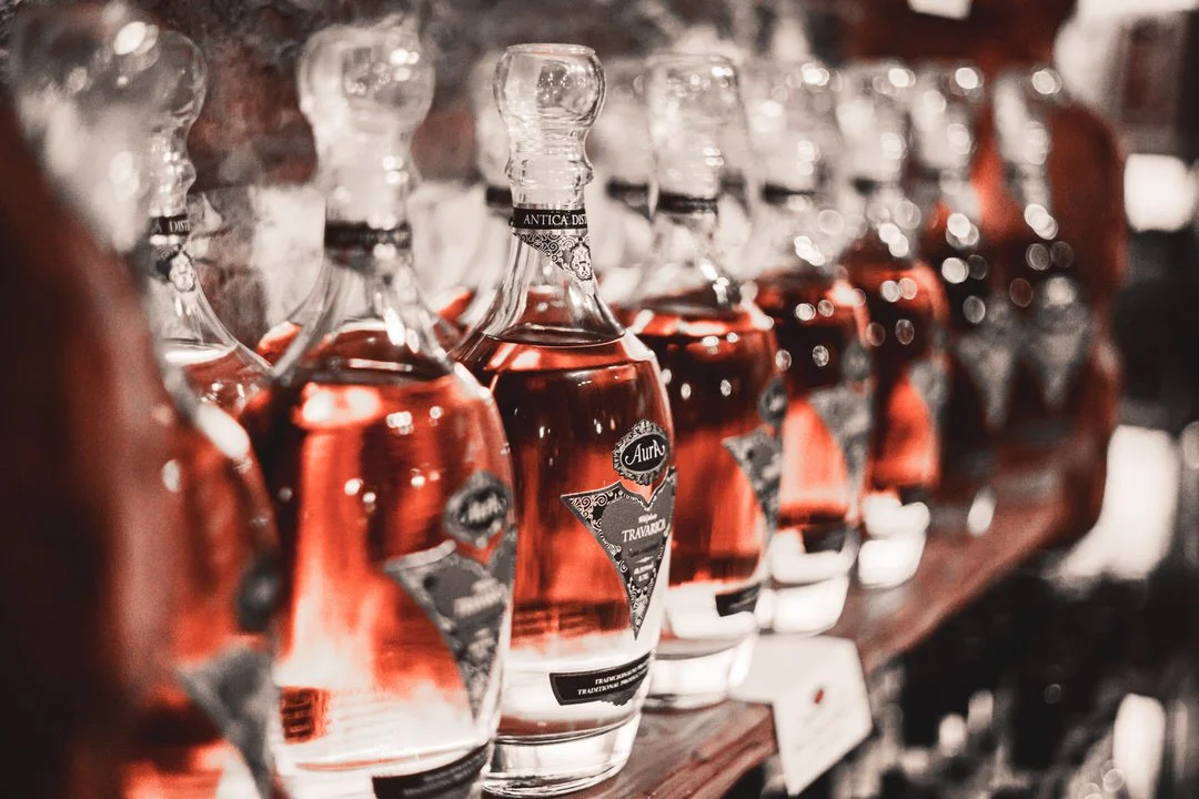 Rows of glass bottles filled with rose-colored liquid on a wooden shelf in a liquor store at Aura Buzet, Croatia.