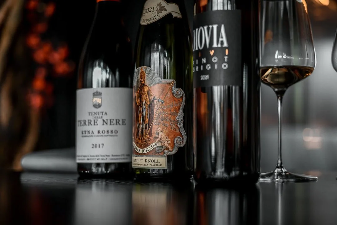 Several bottles of wine and a glass of red wine on a dark reflective surface.