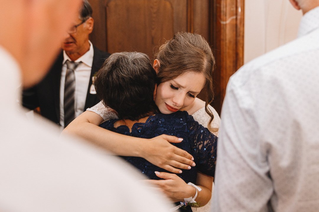 A young woman is hugging an older woman during a heartfelt embrace at a formal event, surrounded by other people.