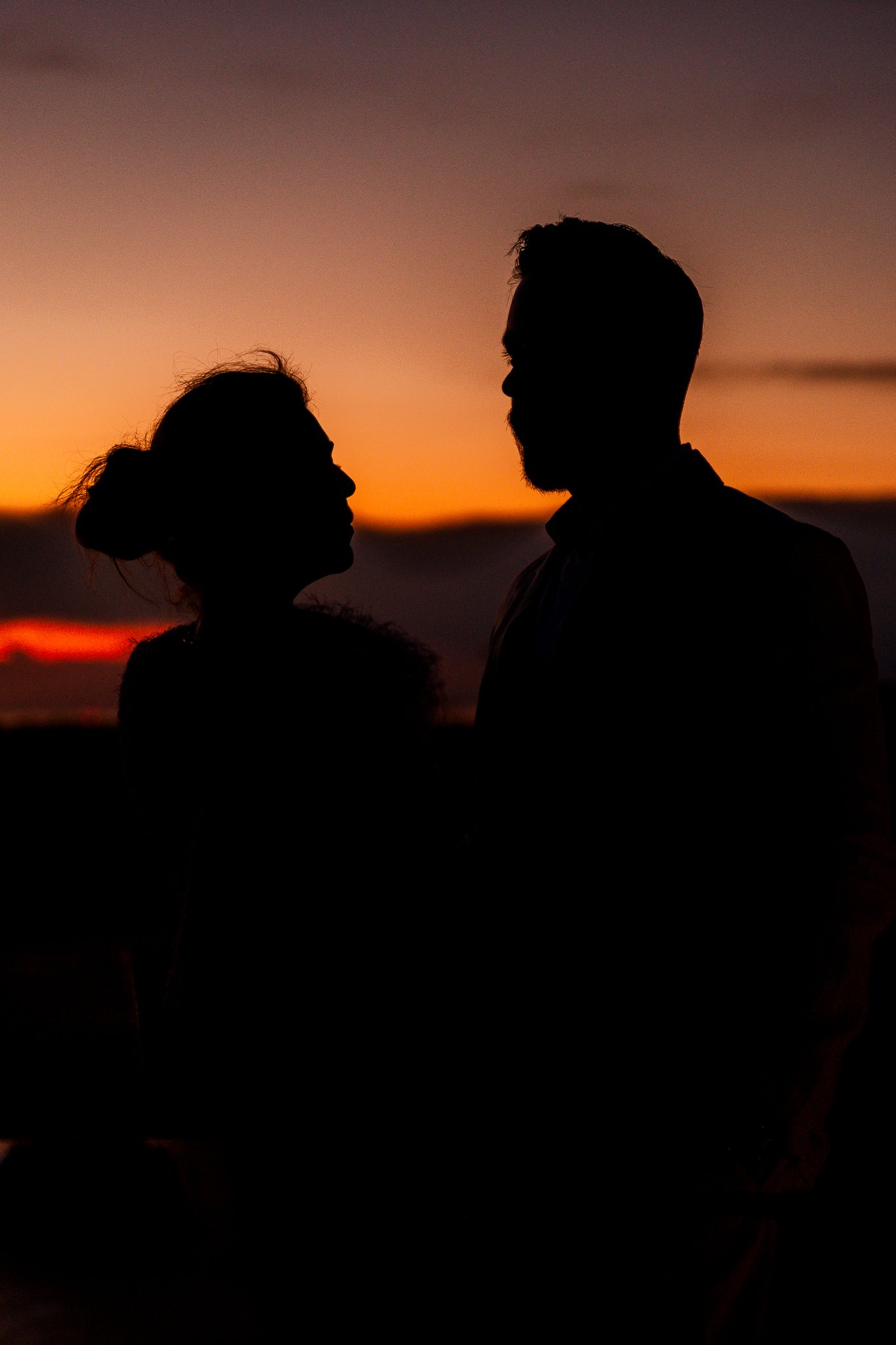 Silhouette of a man and woman facing each other against a sunset sky.