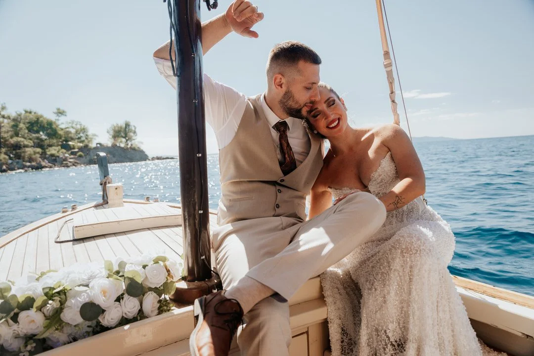 Bride and groom sitting on the deck of a boat cruising around Opatija and Volosko on Kvarner Bay, sharing a tender wedding moment with the Adriatic sea and distant shoreline in the background.