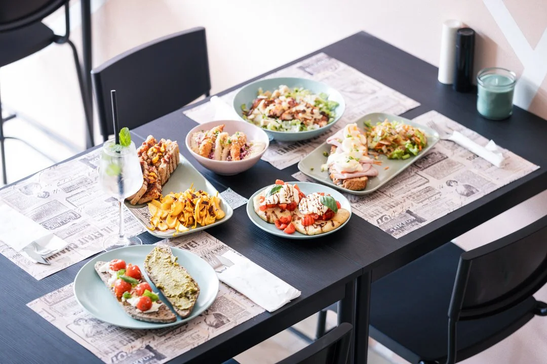 A table set with various plates of colorful dishes, including salad, pasta, pizza, sandwiches, cake, and a cocktail drink, in a dining setting at brunch place in Zagreb Croatia