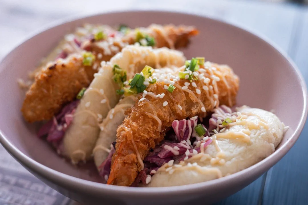 Bowl of fish tacos topped with chopped green onions and shredded cheese, with side of mashed potatoes.