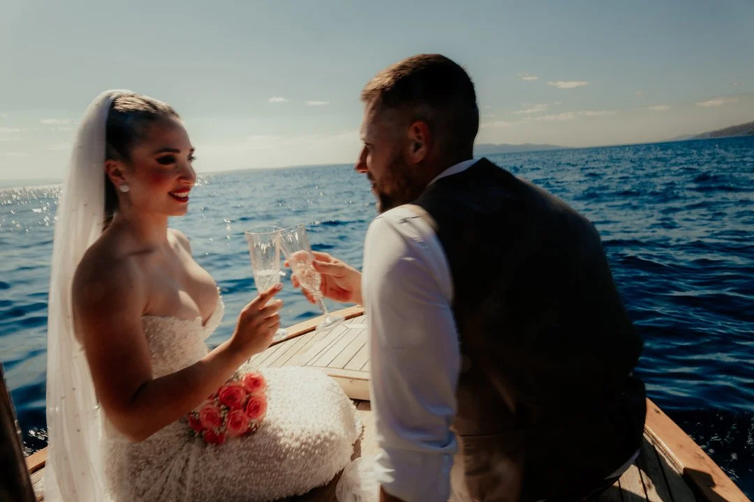 Bride and groom in wedding attire sharing a toast with champagne on a boat at the Adriatic sea.