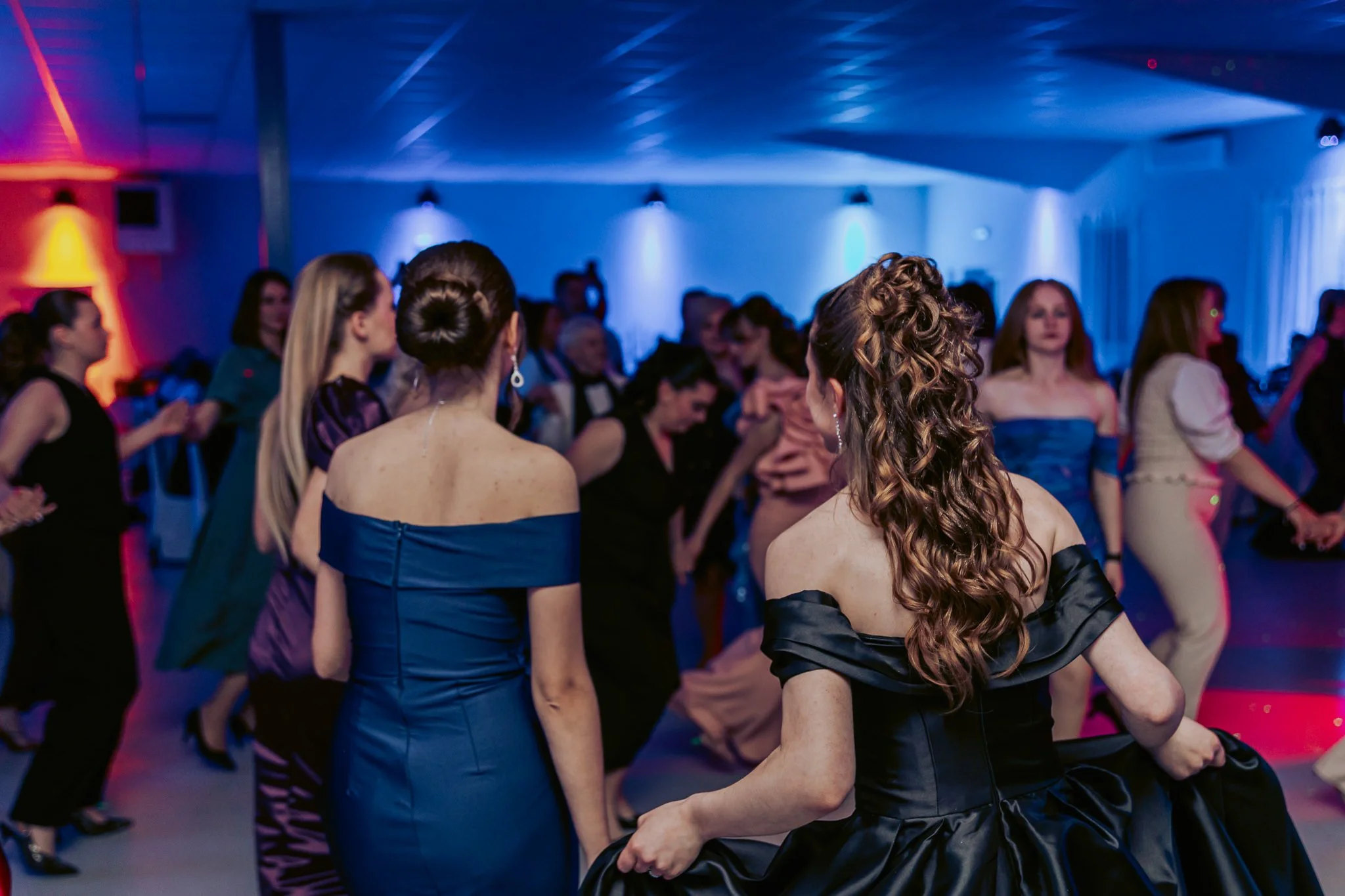 People dancing at a formal event with colorful lighting and elegant attire.