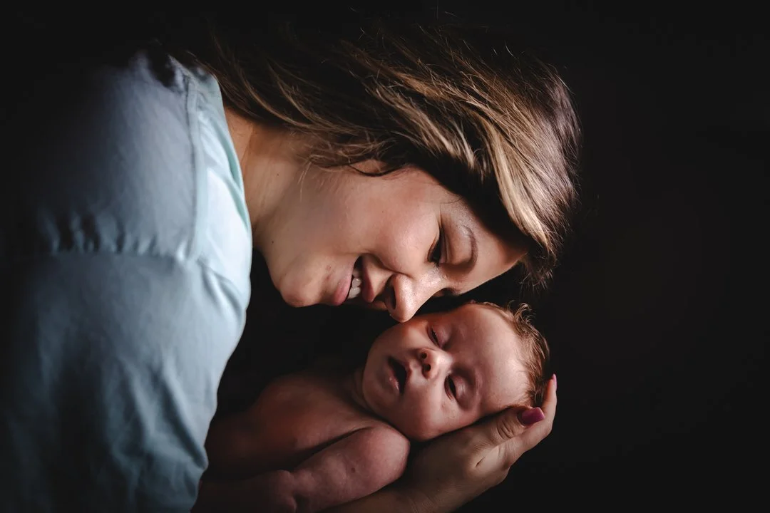 A woman holding a newborn baby close to her face, both smiling and looking at each other against a dark background in zagreb croatia