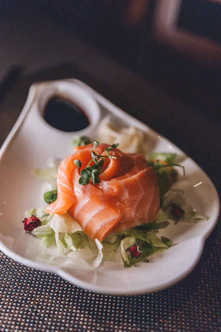 Salmon sashimi on a bed of shredded lettuce, garnished with microgreens, served with soy sauce and wasabi on a ceramic dish in Aera restaurant, Bobingen Germany