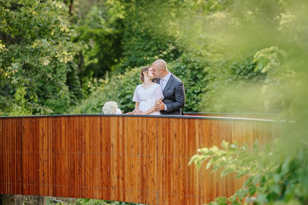 A couple sharing a kiss on a wooden bridge surrounded by greenery during daytime in Vukovar