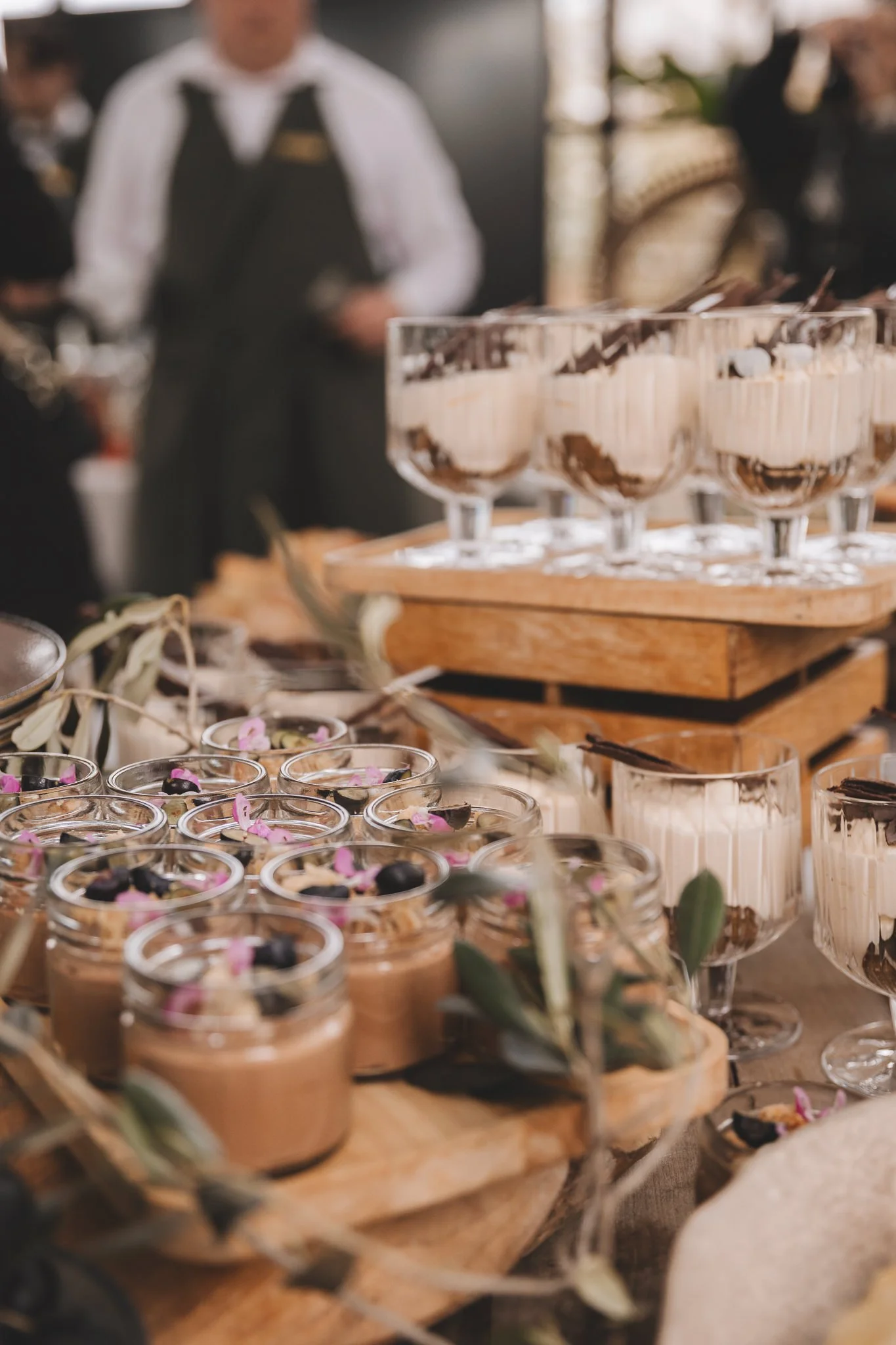 Close-up of small glass cups filled with layered dessert topped with pink flower petals, set on a wooden serving tray at a buffet or event in san canzian istria croatia