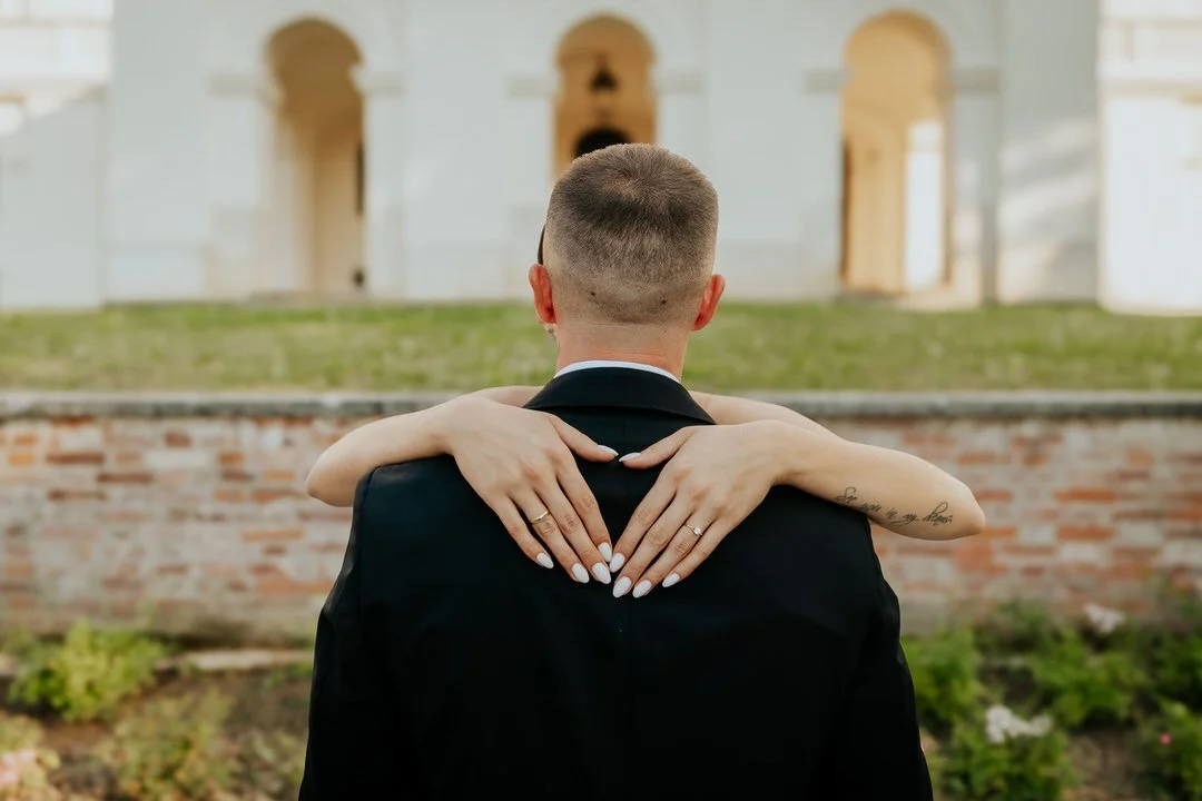 A couple hugging in front of a Pejačević Castle in Našice, with the woman’s arms around the man’s neck and her hands resting on his shoulders.