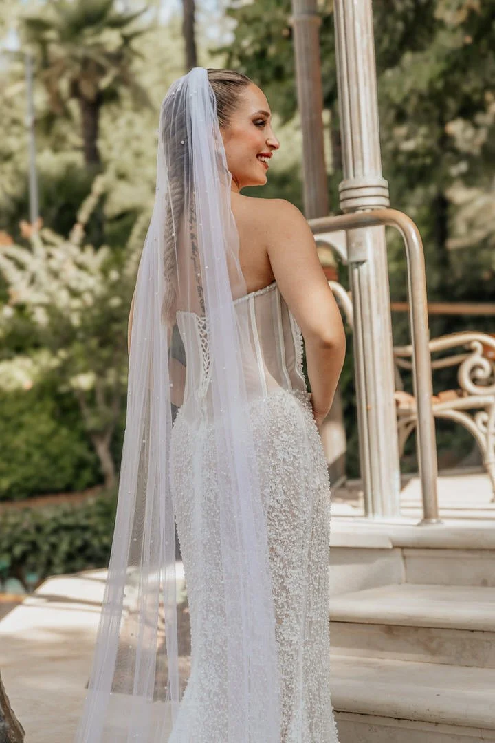 Bridal woman in wedding gown with veil smiling outdoors near a staircase and metal railing.