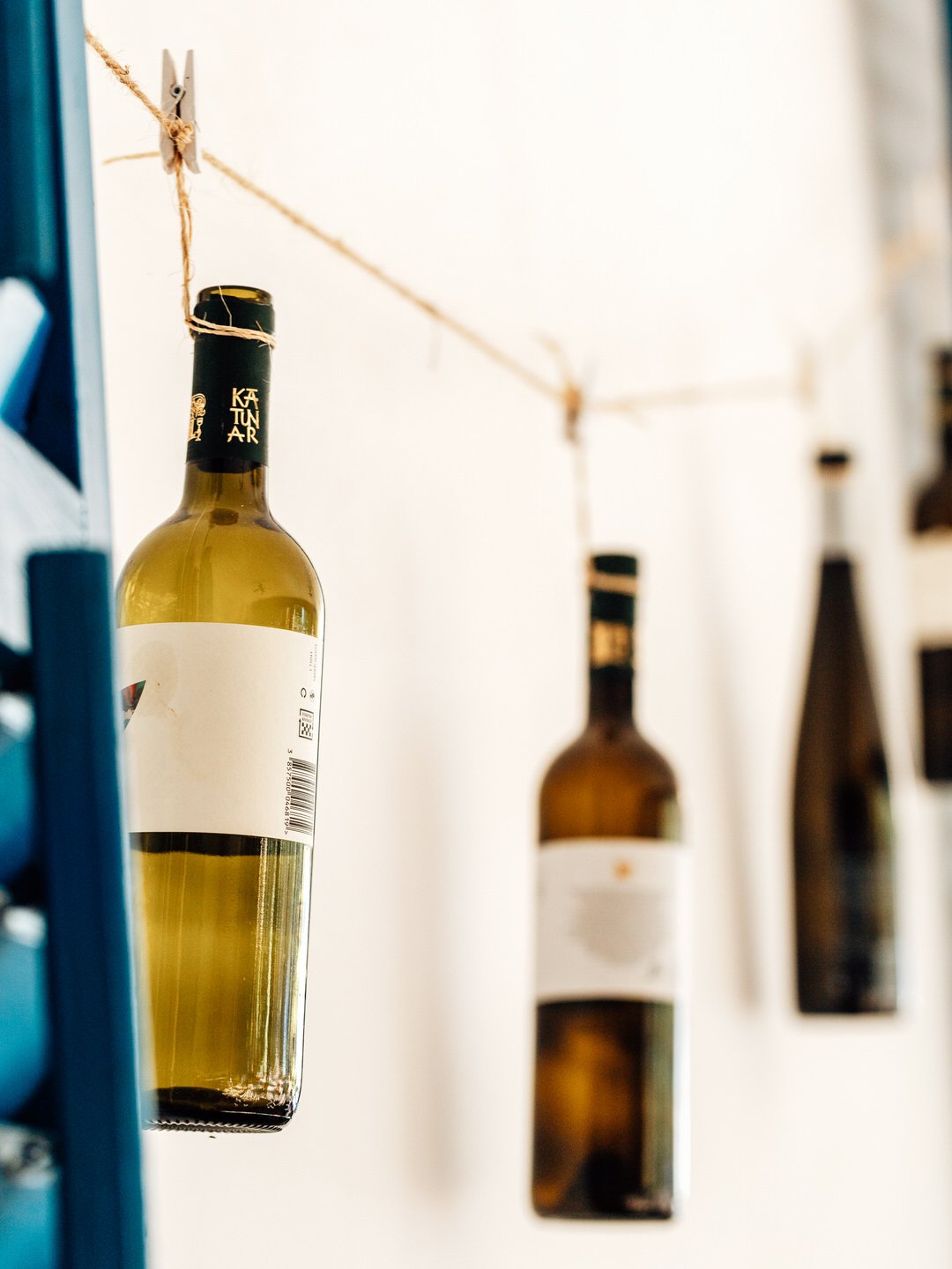 Two wine bottles hanging upside down from a string tied with clothespins, against a white wall.