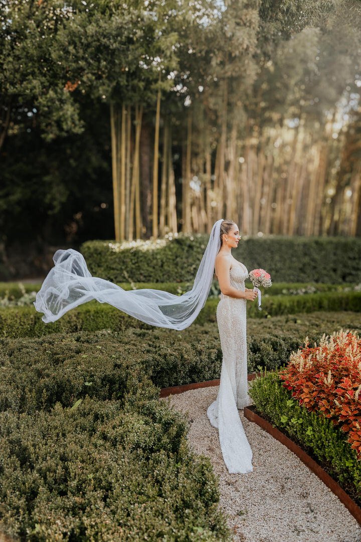 Bride in a white wedding gown and long veil holding a bouquet in Park Angiolina, Opatija, Kvarner, surrounded by green hedges and trees.