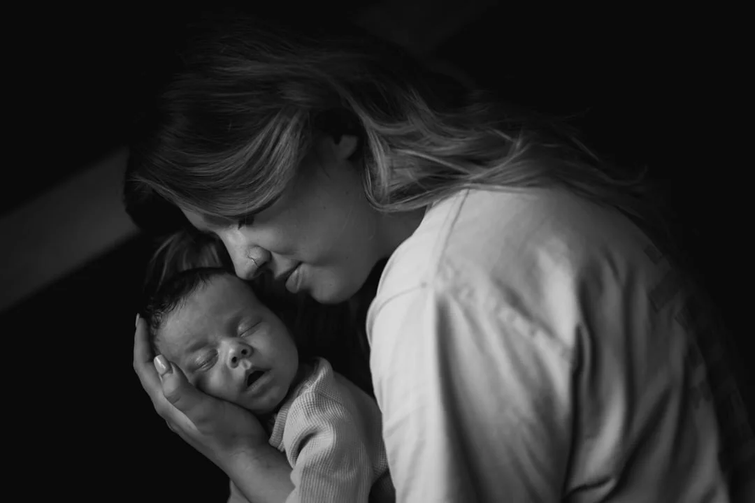 Black and white photo of a woman tenderly holding a sleeping baby close to her face.