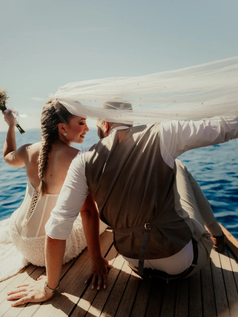 Bride and groom sharing a joyful wedding photoshoot on a boat cruising along the Opatija coast and Kvarner Bay, with the bride holding her bouquet and her veil blowing in the wind.