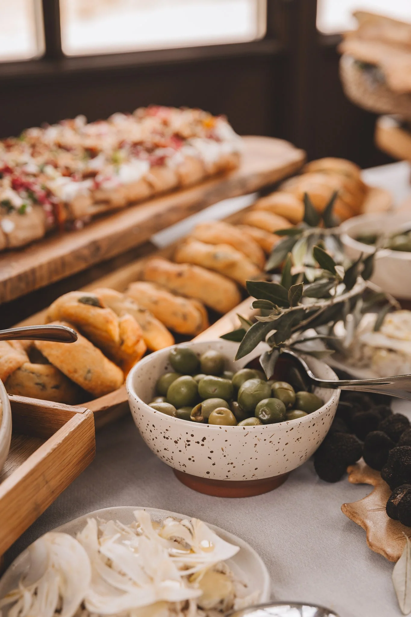 A table with various bowls and platters of food, including a bowl of green olives, baked bread rolls, and other dishes from a San Canzian brunch in Croatia.