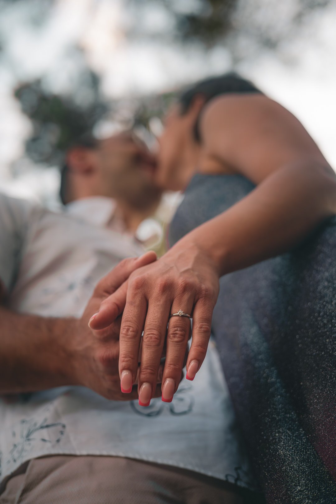 A close-up of a newly engaged couple kissing, with focus on the woman's left hand wearing an engagement ring.