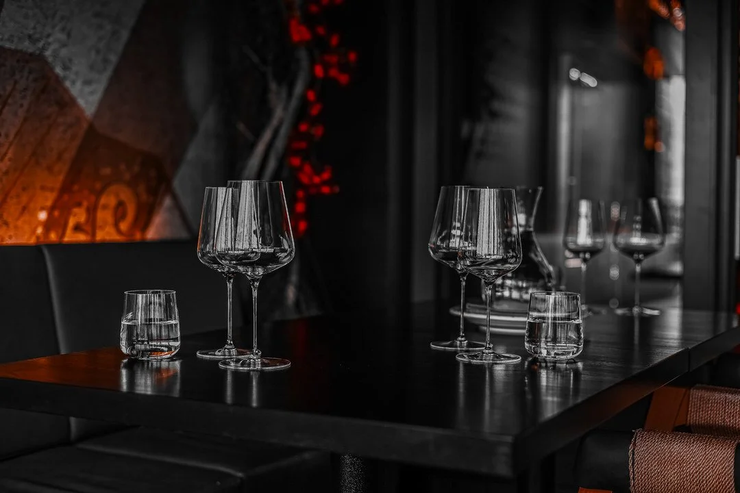 Empty restaurant table with wine glasses and water glasses, dim lighting, dark background with red and orange accents.
