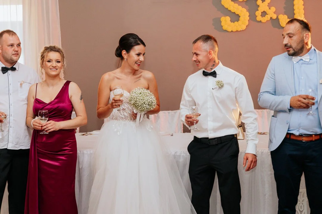 Bride and groom smiling and talking with three other guests at a wedding reception, holding glasses of champagne.