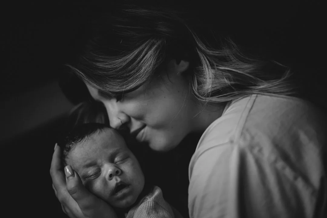 A mother gently holding a sleeping baby with her face close to the baby's head in a black and white photo in Zagreb croatia
