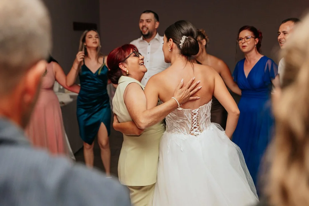 A bride dancing with a woman at her wedding reception surrounded by friends and family.