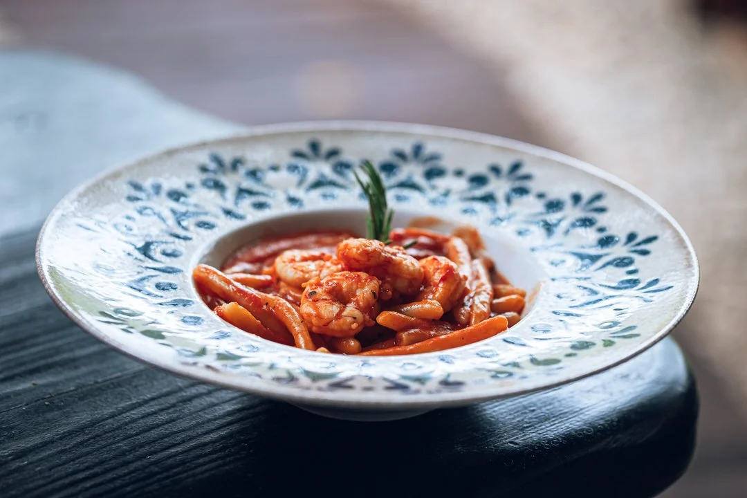 A bowl of shrimp and pasta in tomato sauce garnished with a sprig of green herb.