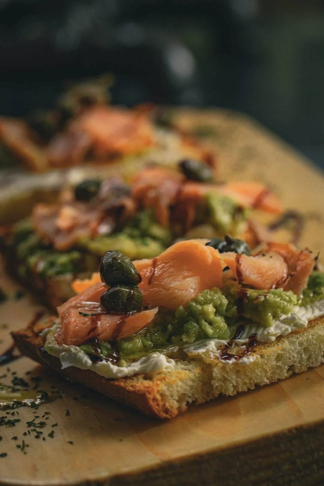 Close-up of an open-faced sandwich with smoked salmon, green pea mash, black caviar, and herbs on toasted bread