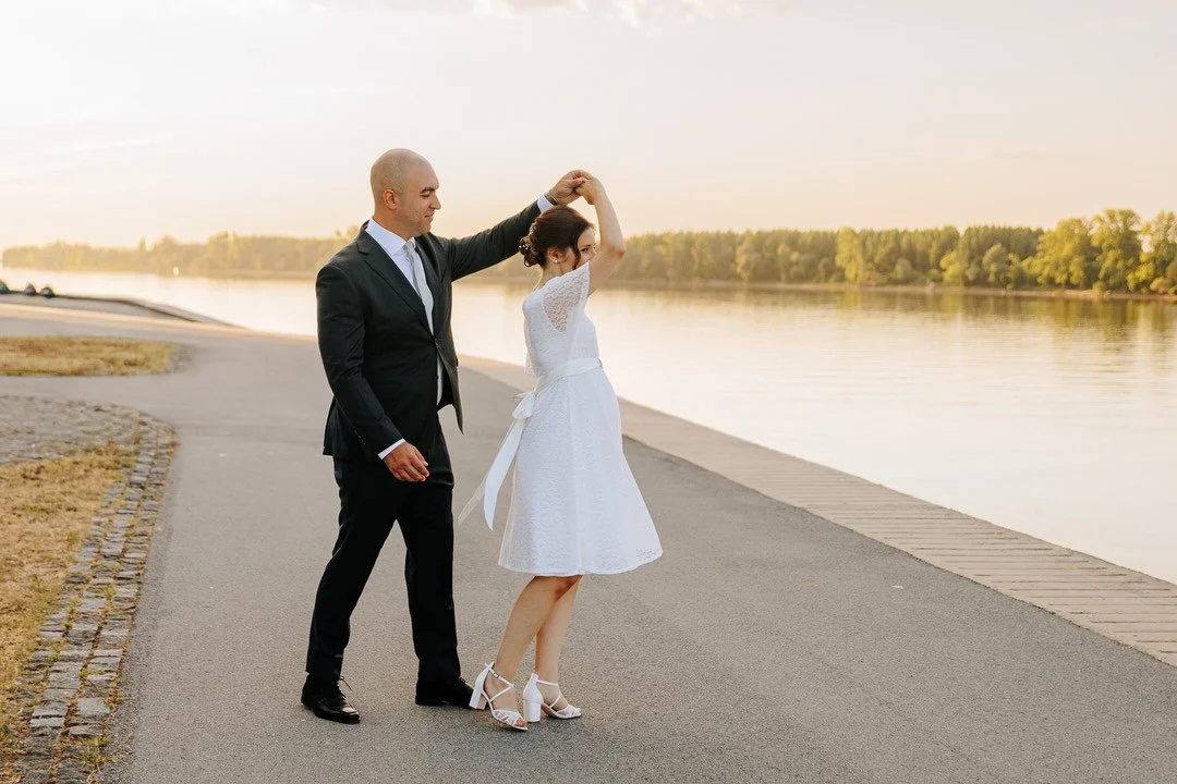 Bride and groom dancing by the Danube River at sunset in Vukovar, Croatia, with trees and golden evening light in the background.