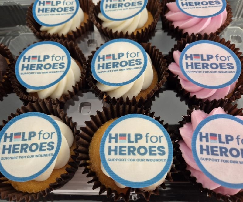 Assorted cupcakes with white and pink frosting, each topped with a round edible topper reading 'Help for Heroes' supporting wounded veterans.